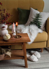 A burning candle in a brass candlestick, Christmas decor on an oak bench, slippers on the carpet...