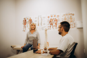 Medical assistant pointing at spine bones to explain diagnosis to senior woman for healthcare.