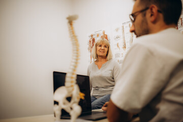 Medical assistant pointing at spine bones to explain diagnosis to senior woman for healthcare.