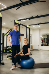 man and woman wearing physiotherapist uniform having rehab session using fit ball at rehab center