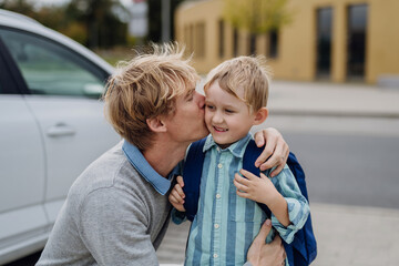 Father saying goodbyeto to son in front of school building, hugging him and kissing him on the...