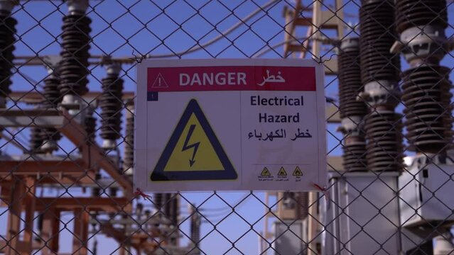 Electrical Safety Warning: Danger Sign for Electrical Hazard in Multiple Languages on Chain-Link Fence at Power Substation