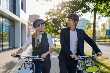 Colleagues commuting through the city, talking and walking by bike on street. Middle-aged city...