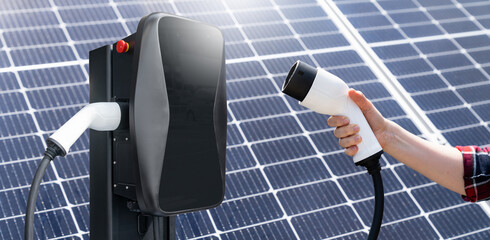 Hand with electric vehicles charging plug on a background of solar panel.