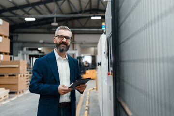 Portrait of male project manager standing in modern industrial factory. Manufacturing facility with...
