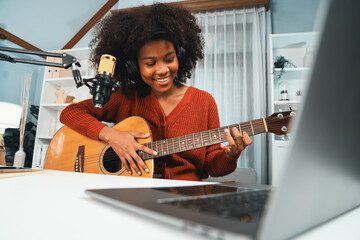 Host channel in musician of young African American playing guitar along with singing, broadcasting on laptop in studio. Decoration of equipment of headsets and recording microphone. Tastemaker. - obrazy, fototapety, plakaty