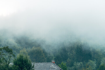 Fog clouds over a mountain house in slovenian Julian Alps forest landscape