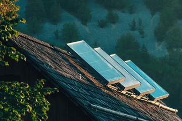 Old solar water heating panels on house roof top in alpine countryside