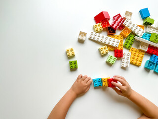 Child playing with colorful building blocks on white background. Top view