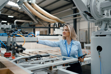 Female engineer in modern industrial factory, checking robotic arm, controling process and...