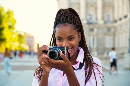 Cuban female tourist smiling and looking at camera while taking photos with a camera sightseeing in Madrid, Spain.