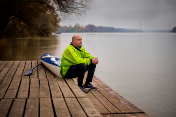 A middle-aged man sitting on the jetty and ready to go kayaking