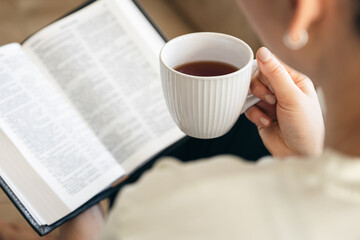 Close up, young woman drinking hot tea and reading favorite paper book.