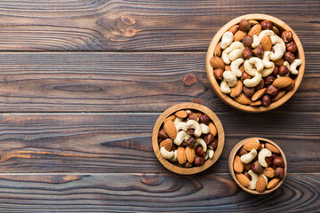 Fototapeta na wymiar Assortment of nuts in wooden bowl on colored table. Cashew, hazelnuts, walnuts, almonds. Mix of nuts Top view with copy space
