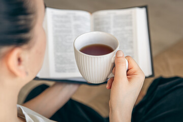 Close up, young woman drinking hot tea and reading favorite paper book.
