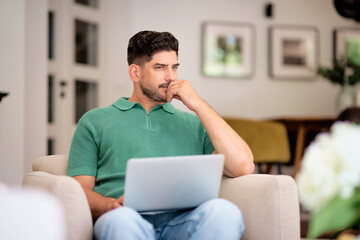Confident mid aged man sitting in an armchair at home and using laptop for work