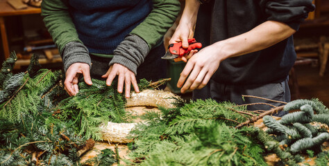 Hände von zwei Menschen halten Draht, Zange und Adventskranz. Mensch bastelt einen weihnachtlichen...