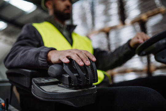 Close up of warehouse worker driving forklift. Warehouse worker preparing products for shipmennt, delivery, checking stock in warehouse.