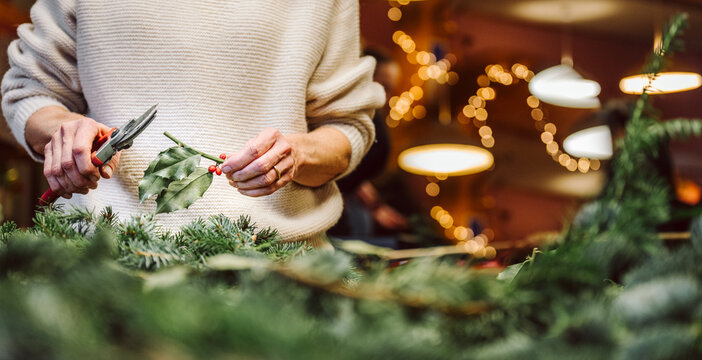 H&auml;nde halten Zange und Teil von Ilex. Mensch bastelt einen weihnachtlichen Adventskranz. Web Banner, Panorama.