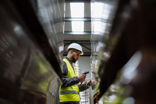 Warehouse worker holding scanner, scanning the barcodes on products in warehouse. Warehouse manager using warehouse scanning system.