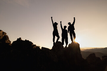 Happy friends hikers or tourists stands with raised arms on mountain top against mountains and...