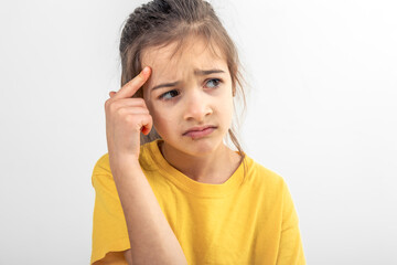Little girl thinking, holding finger at temple, isolated on white background.