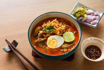 Northern Thai style curried noodle soup with beef and egg on wooden table