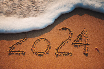 Happy New Year 2024 concept, lettering on the beach sand and splashing wave as nature background