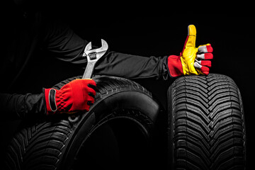 Winter car tires service and hands of mechanic with wrench, screwdriver on black background.