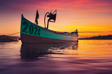 2024 Fishing boat on beach shore and sunset reflection in water  - obrazy, fototapety, plakaty