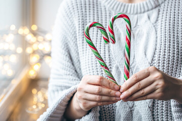 Close up of female hands holding candy canes in the form of heart.