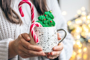 A cup of hot drink with gingerbread and candies in female hands, close up.