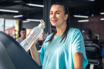 Woman drinking water after exercising on treadmill in gym.