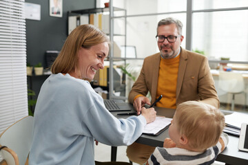 Happy woman filing application for maternity leave while having meeting with social worker in office