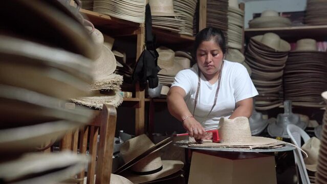 An adult Hispanic woman is cutting the brim of a traditional natural fiber hat