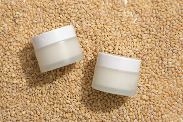 Cosmetic jars with empty label placed on a pile of wheat seeds. Flat lay for mockup design. Rice...