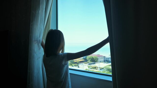 Girl openning window curtains and looking to the horizon. The beginning of the day concept. 4k video footage