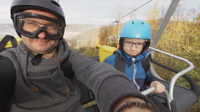 Father and son with safety equipment sitting on cable chair lifting on mountain