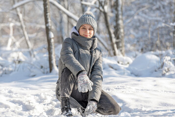 Fototapeta na wymiar Teenage Girl Sits And Poses For A Photo In A Snow-Covered Forest In Winter