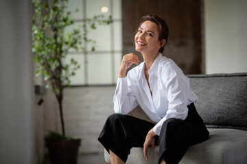 Portrait of an attractive woman weairng white shirt and black pants while relaxing in an armchair at home