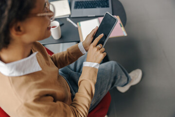 Back view of business woman is using phone sitting in office near window during break time