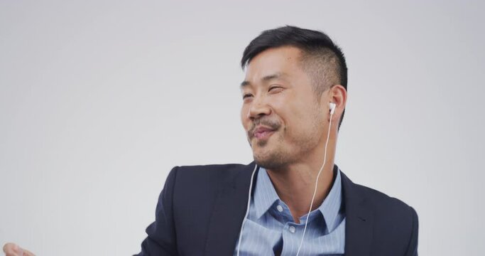 Business man, listening and dance to music for happy energy, streaming service and kpop or celebration in studio. Professional asian person with funny face, earphones and excited on white background
