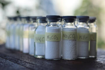 Potassium and sodium carbonates in glass tubes on a background of other white powder reagents.