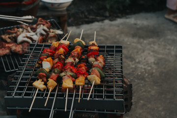 People are cooking seafood and vegetable skewers on a charcoal grill. with a plate of shrimp placed next to it A warm family holiday celebration. BBQ party