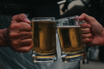 two hands holding frosty mugs of beer, one full and one half-empty, during what appears to be a...