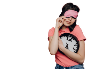Sleepy girl in casual clothes with sleeping mask on face holds wall clock can’t awake standing against transparent background with copy space. Early morning, time to get up. Time management concept.