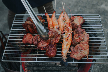 People are cooking seafood and vegetable skewers on a charcoal grill. with a plate of shrimp placed next to it A warm family holiday celebration. BBQ party