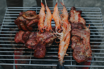 People are cooking seafood and vegetable skewers on a charcoal grill. with a plate of shrimp placed next to it A warm family holiday celebration. BBQ party