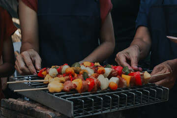 People are cooking seafood and vegetable skewers on a charcoal grill. with a plate of shrimp placed next to it A warm family holiday celebration. BBQ party