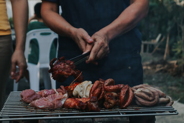People are cooking seafood and vegetable skewers on a charcoal grill. with a plate of shrimp placed next to it A warm family holiday celebration. BBQ party